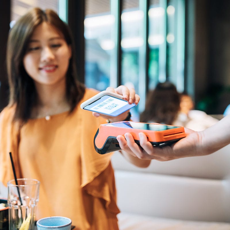 Asian Young Woman Paying With Smartphone In A Cafe.