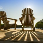 Sunrise on two empty Adirondack chairs sitting on a dock.