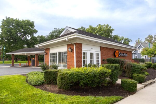 A brick building with large windows houses a Byline Bank branch, surrounded by trimmed bushes and a drive-through area on the left.
