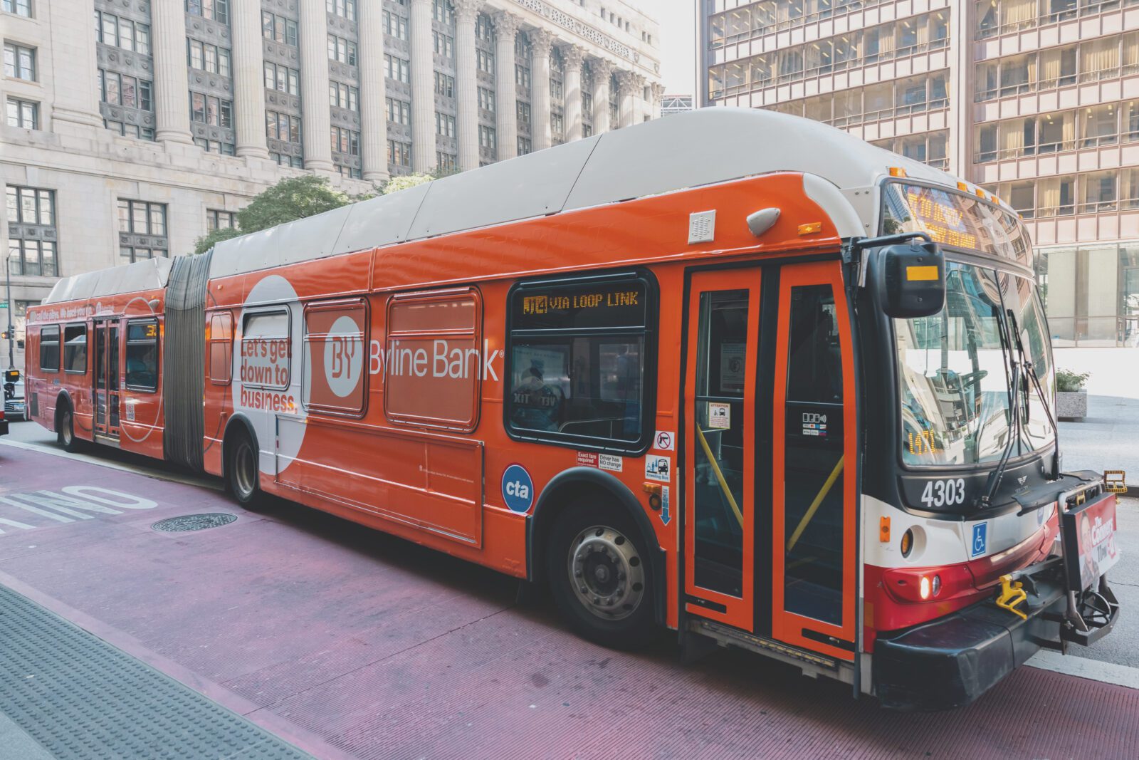 An orange articulated city bus with Byline Bank advertising, stopped on a downtown street in Chicago.