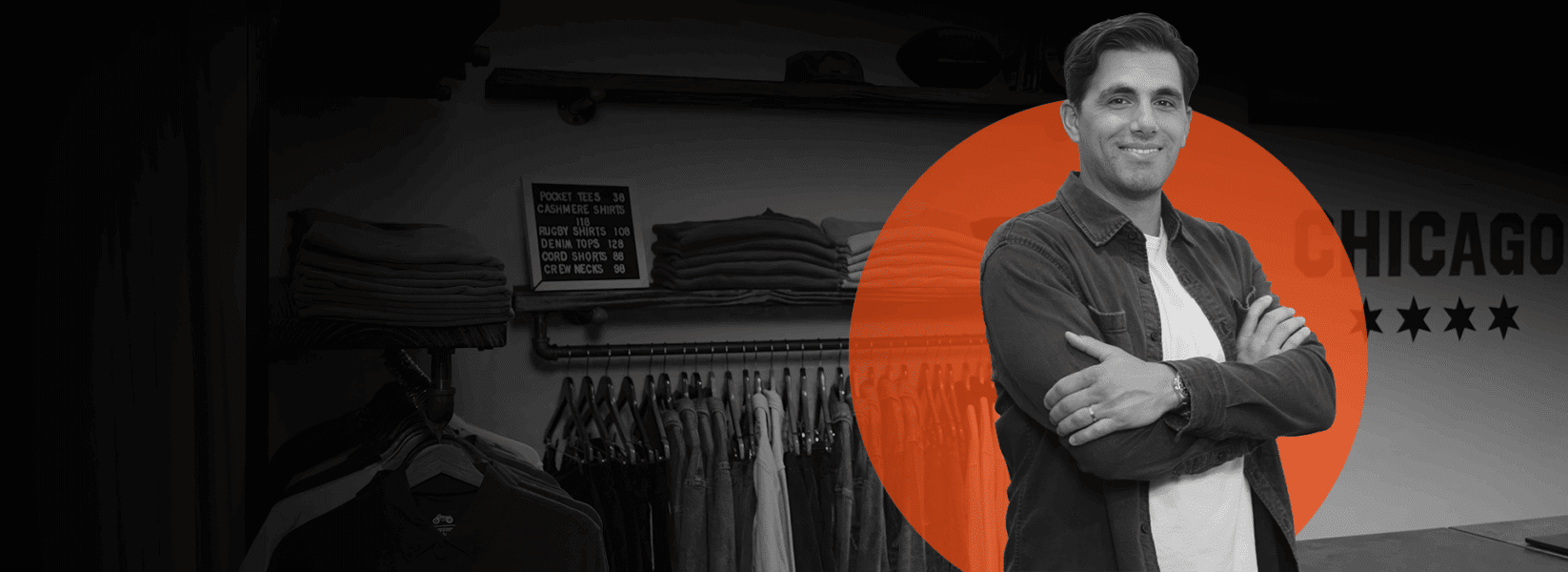 Man standing with arms crossed in a clothing store, facing the camera. He is highlighted by an orange circle; folded clothes and hanging garments are visible in the background.