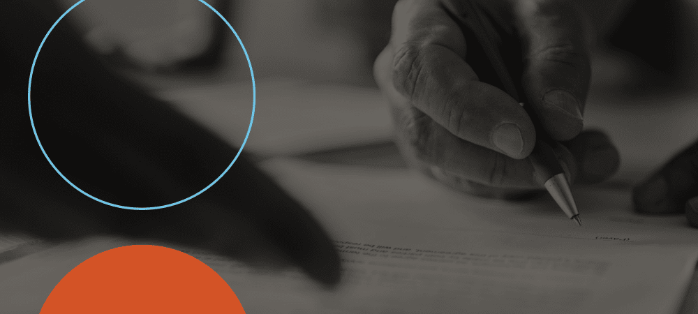 A close-up of two hands over paperwork, one hand holding a pen, with a blue circle and an orange semicircle overlay on the image.