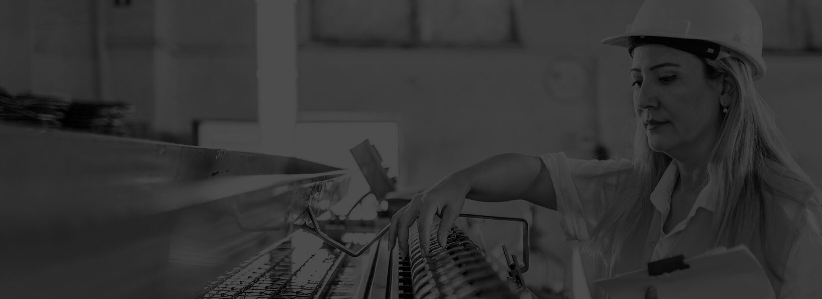 Woman wearing a hard hat and holding a clipboard inspects machinery in an industrial setting.