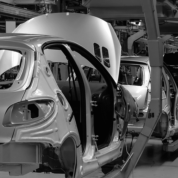 Partially assembled cars with open hoods and doors are lined up on an automotive factory production line in black and white.