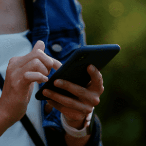 A person holding a smartphone and using their index finger to touch the screen, wearing a white shirt, blue jacket, and a smartwatch.