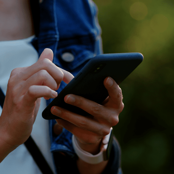 A person holding a smartphone and using their index finger to touch the screen, wearing a white shirt, blue jacket, and a smartwatch.