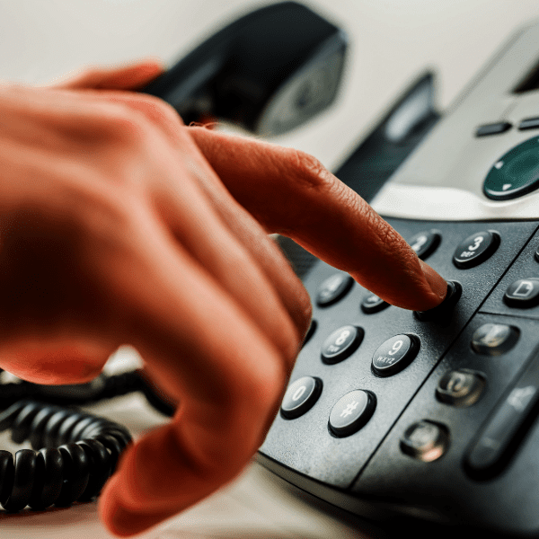 A hand is dialing a number on a black office landline phone with a corded handset.