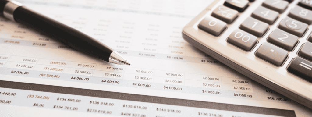 A close-up of a pen and calculator resting on a financial spreadsheet with rows of numbers.