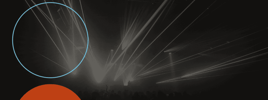 A dark concert stage with bright white spotlights and laser beams cutting through smoke; a large blue circle and a partial red circle overlay the image.