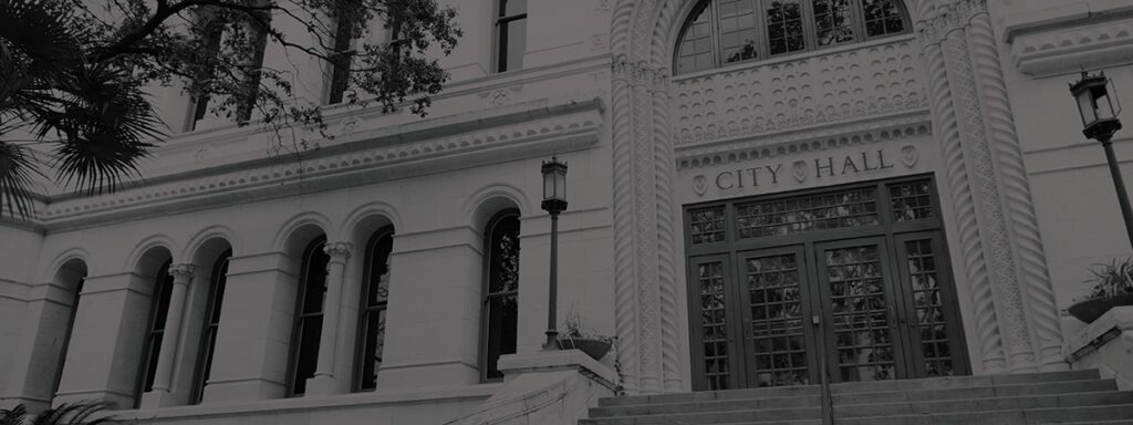Exterior view of a building with arched windows, decorative columns, and an entrance labeled “City Hall” above double doors.