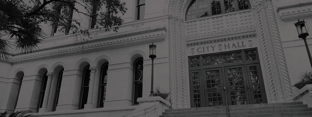 Exterior view of a building with arched windows, decorative columns, and an entrance labeled “City Hall” above double doors.