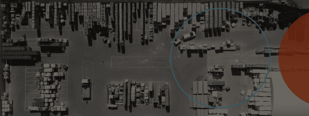 Aerial view of an industrial storage yard with organized rows of materials, several parked vehicles, and a large blue circle overlay on the right.
